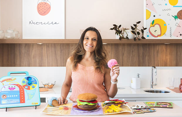 Renata Riciati à mesa do consultório com brinquedos de comida
