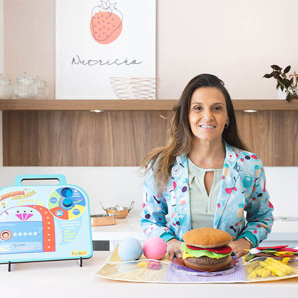 Renata Riciati no consultório, com brinquedos de comida sobre a mesa