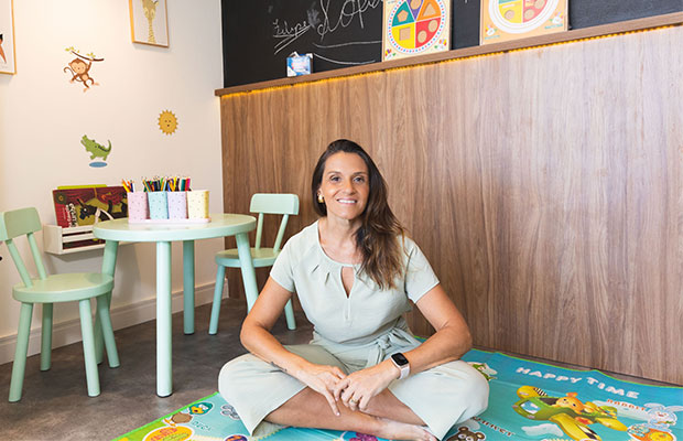 Sala do consultório com mesinha infantil, cadeiras verdes, tapete e brinquedos
